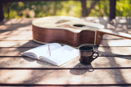 Composer's desk in nature, Coffee cup, notebook, and acoustic guitar placed, Close-up.の写真素材