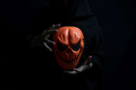 Dark Halloween Concept, Orange ghost mask in hands of devil.の写真素材
