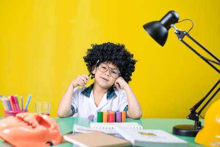 Boy wearing a wig is doing homework, Questionable expression at the desk.の写真素材