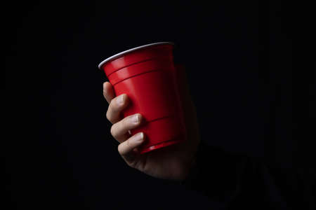 Red plastic cup with a hand in the dark, Close up.の写真素材