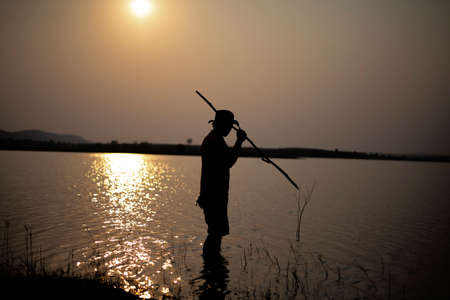 Fisherman silhouette, Man with a gaff stabbed a fish in the twilight.の写真素材