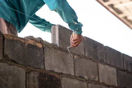 Close-up of professional construction worker laying bricks in industrial site.