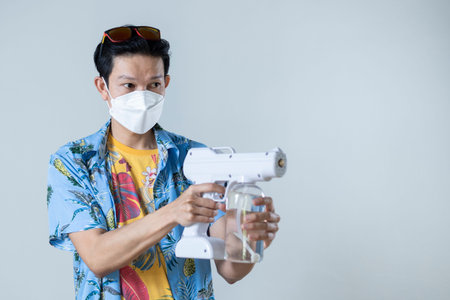 Asian man wearing medical mask holds gun to spray disinfectant, Songkran Festival in Thailand, Under...