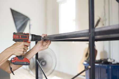 Hand holding an electric drill is drilling steel furniture table, Close up.の写真素材