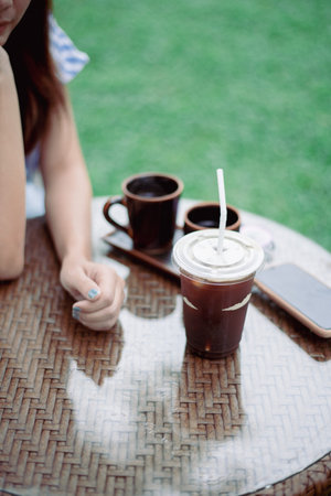 Iced black coffee on the table with a woman's hand placed, close up