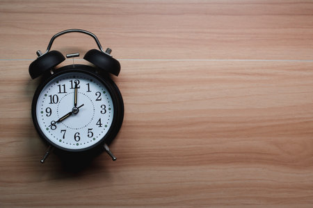 Analog alarm clock is placed on wooden table, Empty space for text.