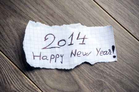 Happy new Year 2014 - Hand writing text on a piece of paper on wood backgroundの写真素材