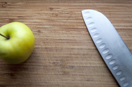 Close up detail of a large knife and a green apple on a wood chopping board.の写真素材