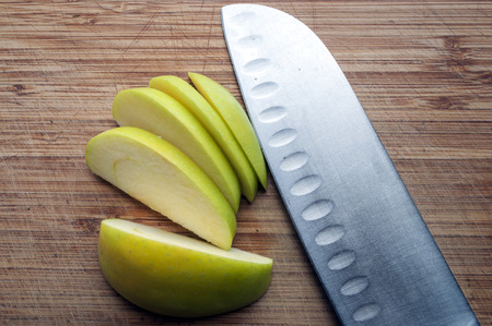 Close up detail of a large knife and a sliced green apple on a wood chopping board.の写真素材