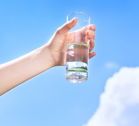 Glass of water in hand on the blue sky with cloudsの写真素材