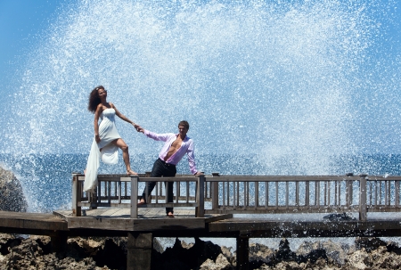 Happy young couple walking on the old pier  Ocean waves beating on the rocksの写真素材