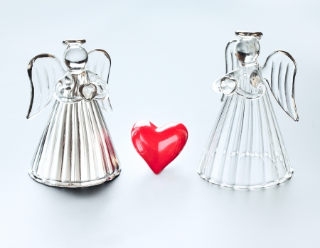 Two angels holding hearts. Between them a big red heart symbol of loveの写真素材