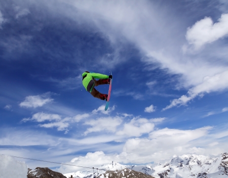 Jumping snowboarder keeps one hand on the snowboard on blue sky backgroundの写真素材