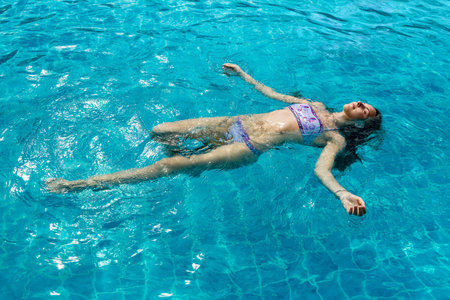 Beautiful young girl floating in pool on his back in hot summer day