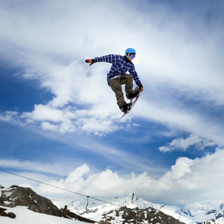 Jumping snowboarder keeps one hand on the snowboard on blue sky backgroundの写真素材