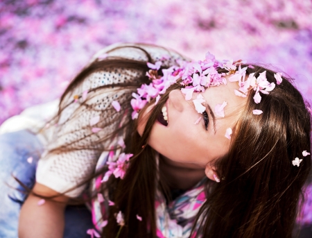 Beautiful Young woman showered pink petals cherry blossoms in the air in spring dayの写真素材