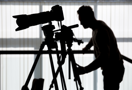 Silhouette of photographer and cameraman shot the video on a tripod at the workplace indoorsの写真素材