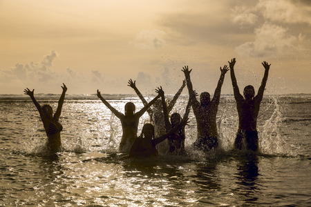Silhouettes of young group of people jumping in ocean at sunsetの写真素材