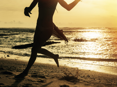 Silhouette of young woman jogging along the ocean shore at sunsetの写真素材