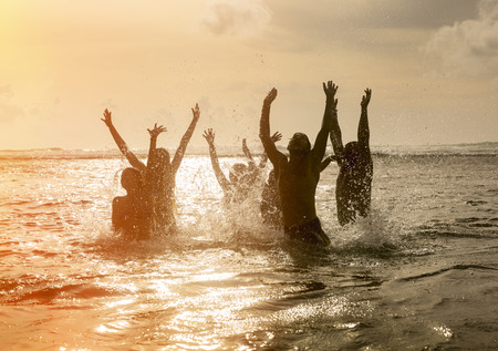 Silhouettes of young group of people jumping in ocean at sunsetの写真素材