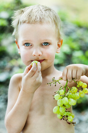 Happy little boy with brush of white grapesの写真素材