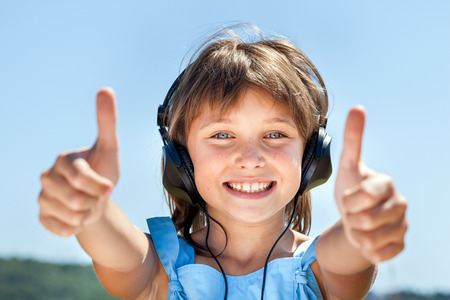 Happy little girl in headphones listens to music against the blue skyの写真素材