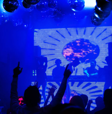 Dj playing on stage. Silhouettes female dancers and people in motion, dancing at nightclub