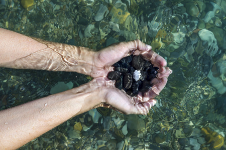 Women's hands with a handful of sea stones under water, holds in the clear sea water. Top viewの写真素材