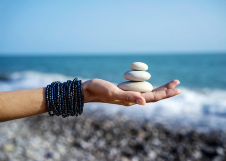 Women's hands holds pyramid of stones on the palm on background of coastline, sea and skyの写真素材