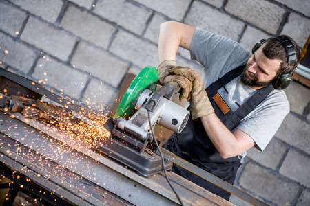 Industrial worker cutting metal with many sharp sparks working on compound mitre saw with circular bladeの写真素材