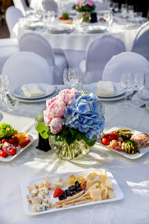 Elegant banquet tables prepared for a conference or a party and covered with a white tablecloth and decorated with flowers for guestsの写真素材