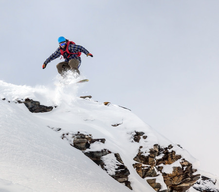 Jumping snowboarder in mountains on the snowboardの写真素材