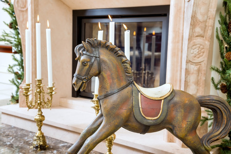 Old wooden rocking horse for children on the background of burning candlesticks in sconces near the fireplaceの写真素材
