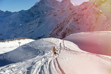 Freerider snowboarder moving down on the background of beautiful Caucasian mountains on Elbrus. Beautiful side effect sunbeamの写真素材