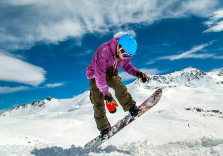 Snowboarder in mountains taking for the edge snowboard against the blue sky and cloudsの写真素材