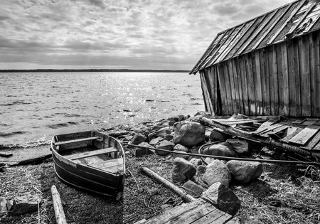 Old wooden fishing boat and barn on lake coast in Karelia. Black and white photoの写真素材