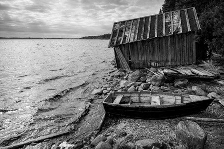 Old wooden fishing boat and barn on lake coast in Karelia. Black and white photoの写真素材