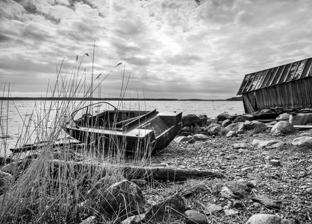 Old wooden fishing boat and barn on lake coast in Karelia. Black and white photoの写真素材