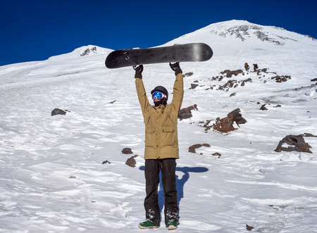 Portrait of snowboarder on background beautiful landscape of snowy high mountains Elbrus standing with raised up snowboardingの写真素材