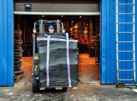 Worker on forklift transporting cargo on large modern warehouseの写真素材