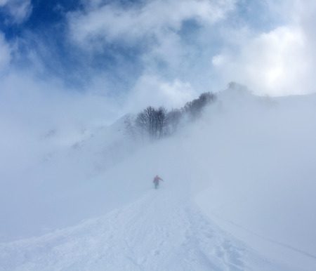 Snowboarder in the mist rises on the mountainside along the road up on background blue sky and cloudsの写真素材