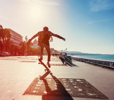 Silhouette of Skateboarder jumping in city on background of promenade and seaの写真素材