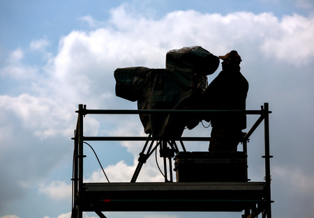 Silhouette of cameraman and video equipment on a tripod at the workplace outdoorsの写真素材