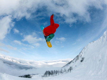Jumping snowboarder keeps one hand on snowboard in mountains in ski resort on blue sky backgroundの写真素材