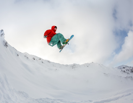 Jumping snowboarder keeps one hand on snowboard in mountains in ski resort on blue sky backgroundの写真素材