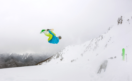 Jumping snowboarder keeps one hand on the snowboard in mountainsの写真素材