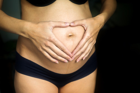 Pregnant woman mother in lingerie with hands on belly forming heart closeupの写真素材