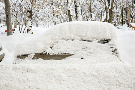 Cars covered with snow in the parking in the yard near a houseの写真素材