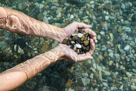 Women's hands with a handful of sea stones under water, holds in the clear sea water. Top viewの写真素材