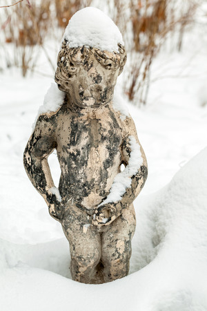 Statue of pissing child boy in country house in winter in the yard, covered with snowの写真素材